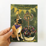 Hand holding greeting card, image of pug with huge cupcake, text says Happy Birthday