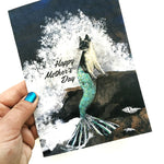 Happy Mother's Day Greeting Card being Held. Image is mixed media illustration of a mermaid cat with waves crashing behind her.